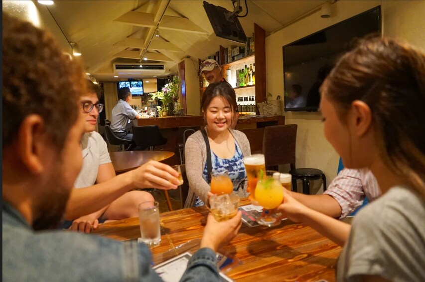 A group of people sitting at a wooden table in a restaurant, holding drinks and toasting. 5