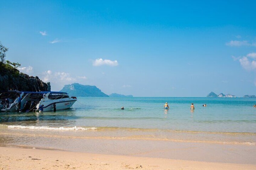 A beach with boats, clear water, and distant mountains. 4