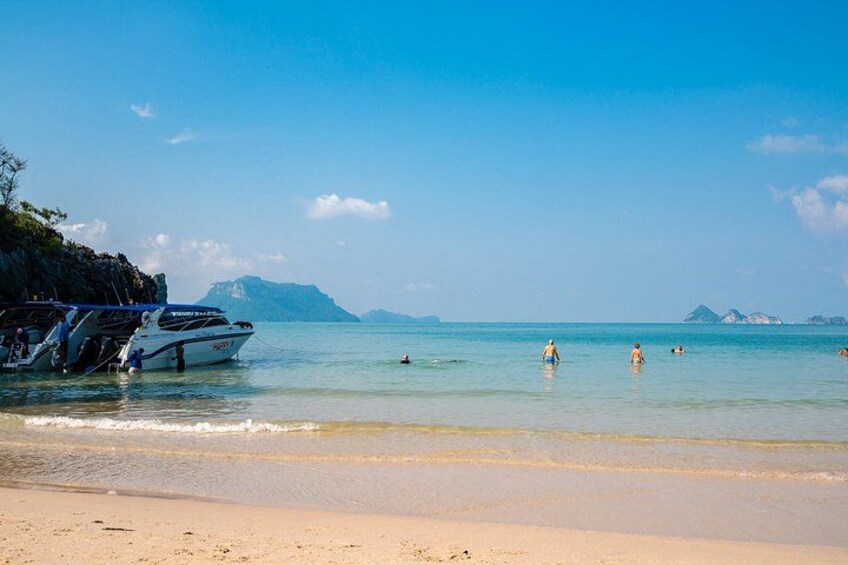 A beach with boats, clear water, and distant mountains. 5