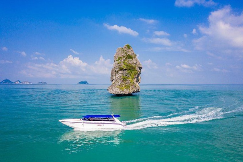 A boat moving through turquoise waters with a large rock formation in the background. 4