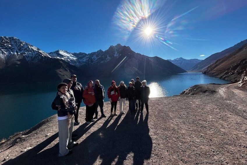 A group of people standing on a mountain path with a lake and snow-capped mountains in the background. 3