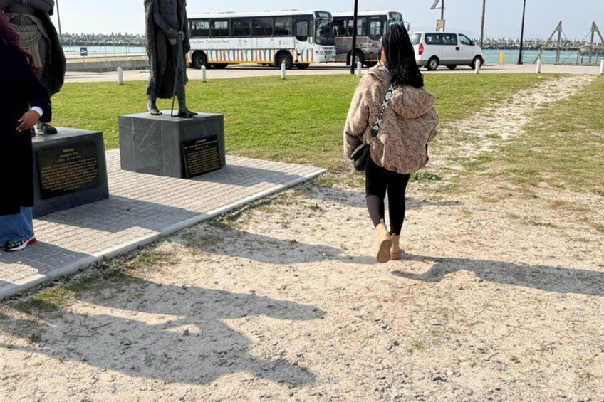 A person walking on a sandy path, a statue, and a bus in the background. 3