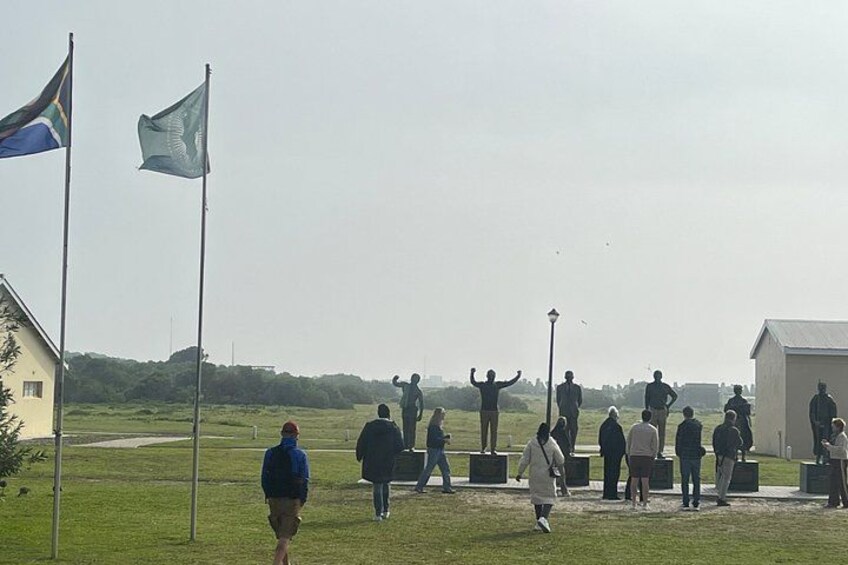 A group of people gathered around a statue in a grassy field with flags and a building in the background. 2