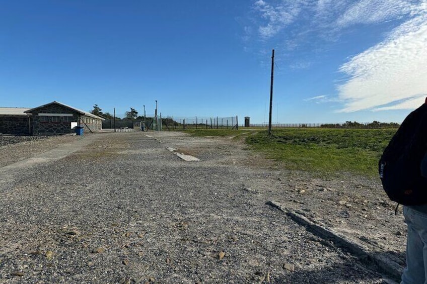 A gravel parking area with a building and a fence in the background. 4