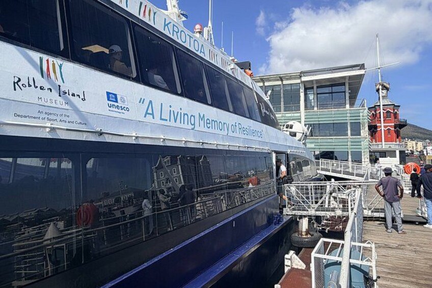 A boat named 'A Living Memory of Resilience' docked at a pier with the 'Robben Island Museum' and 'KROTOA' visible. 3