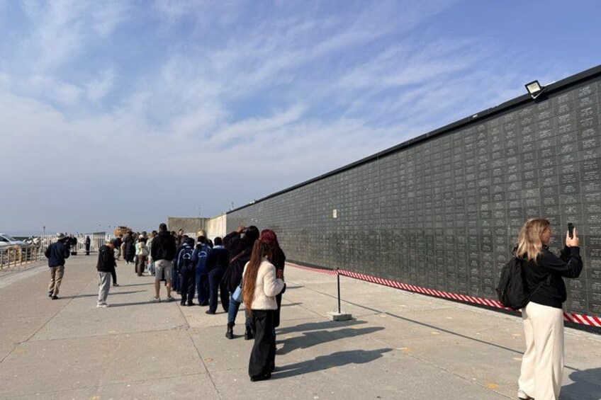 A long wall with names inscribed, a crowd of people, and a clear sky. 4