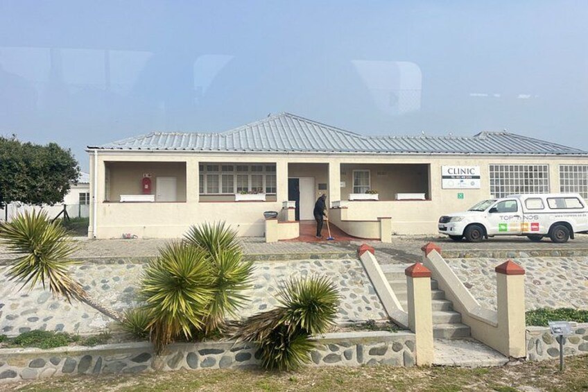Edificio de clínica con techo de tejas, una persona de pie en la entrada y un vehículo blanco estacionado al frente. 4