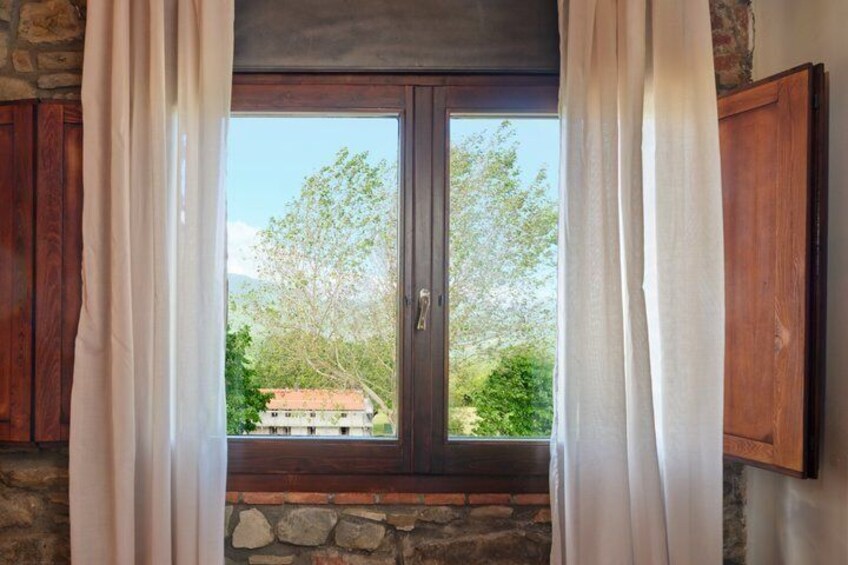 A window with curtains, a stone wall, and a view of trees and a building outside. 2