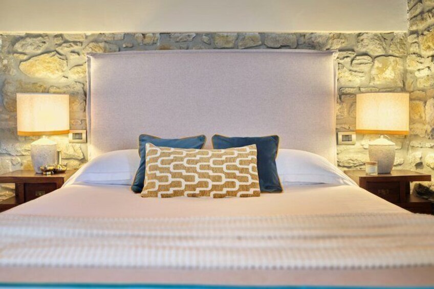 A bed with a stone wall backdrop, two bedside lamps, and patterned pillows. 4