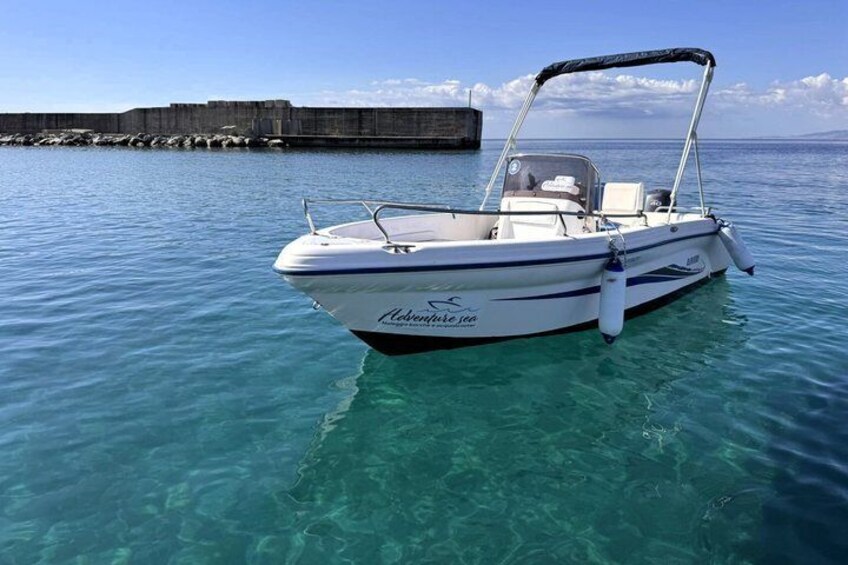 A white motorboat named 'Adventure 35' anchored in clear turquoise water with a rocky breakwater in the background. 2