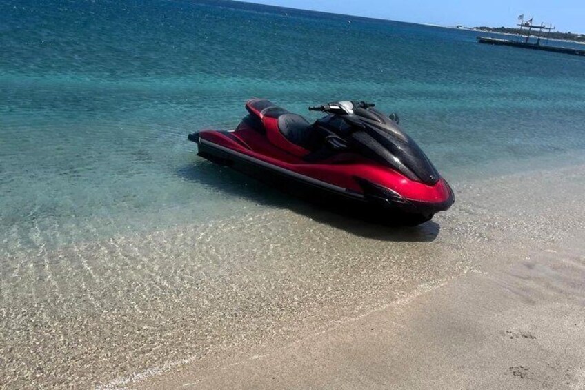 A red jet ski on a clear beach with shallow water and a distant ship. 5