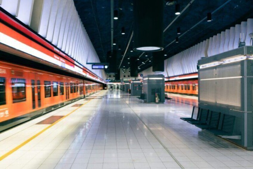 A modern train station with a moving train on the left, a platform, and air conditioning units on the right. 4