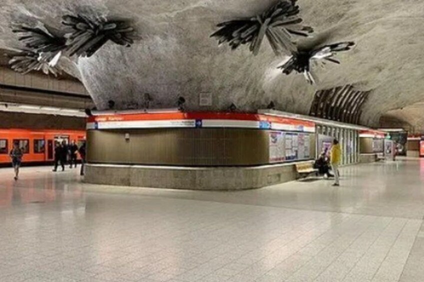 A subway station with a curved ceiling, a central platform, and a train on the left. 3