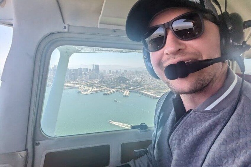 A person in a cockpit with a view of a coastal cityscape and port facilities. 4