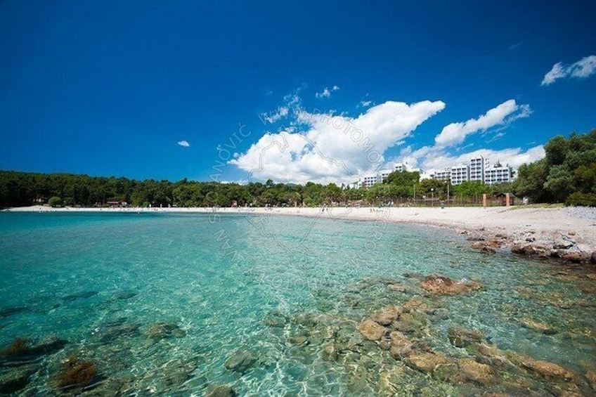 A clear turquoise sea, a sandy beach, and buildings in the background. 5