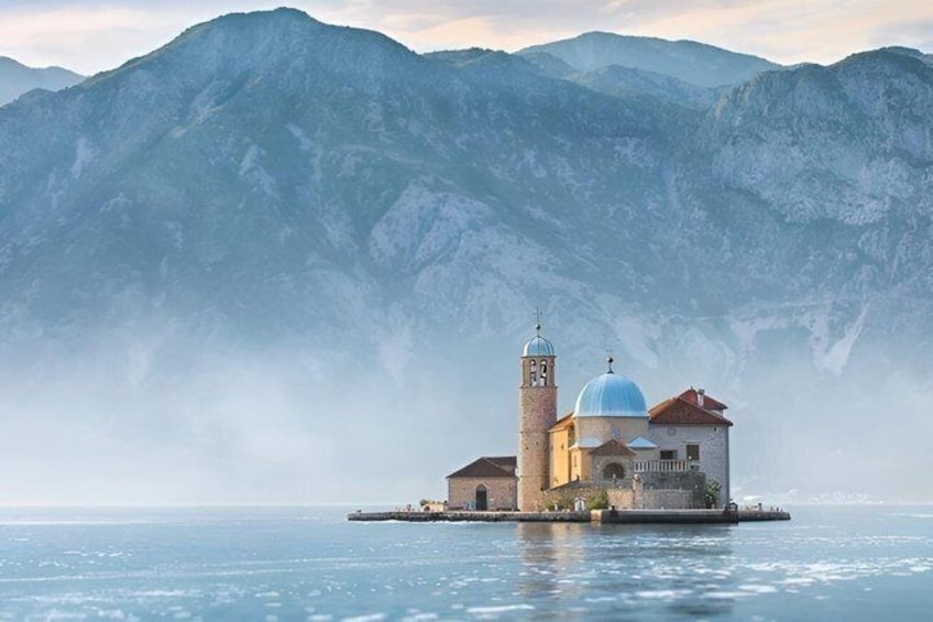 A church on a small island with mountains in the background. 1