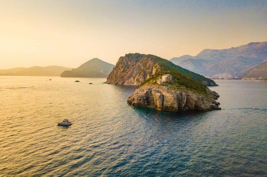 A calm sea with a small island, a boat, and distant mountains. 5