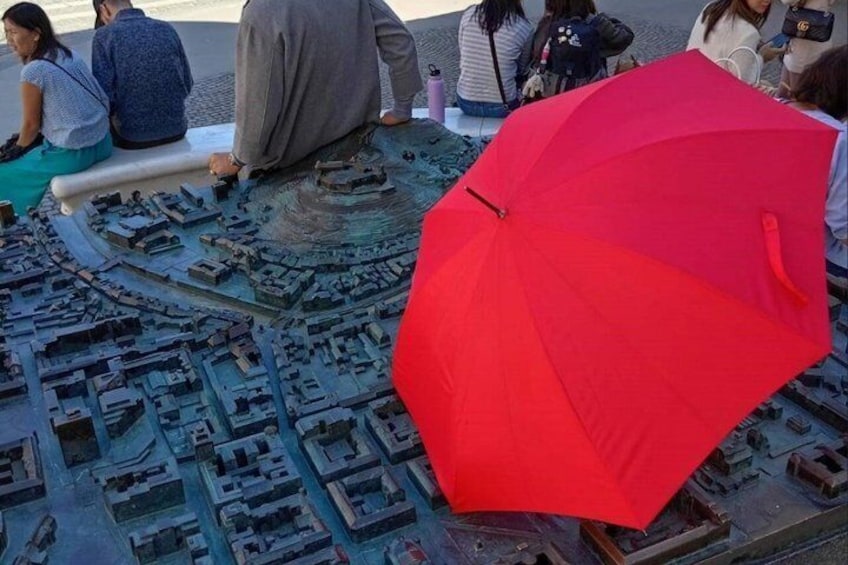 A detailed scale model of a cityscape with a prominent red umbrella in the foreground. 3