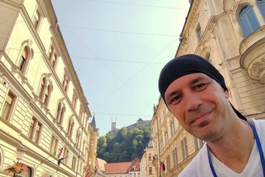 A man in a white shirt and black headband standing in front of a building with classical architecture. 1