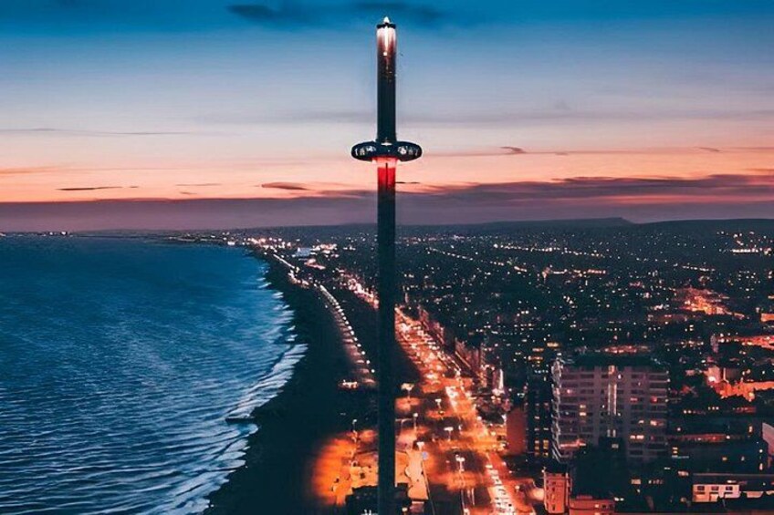 A cityscape at dusk with a prominent tall building in the center, a coastline with waves, and a densely populated area with lights. 1