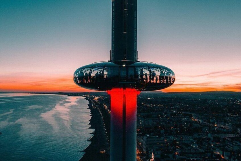 A tall tower with a circular observation deck, overlooking a coastal cityscape at sunset. 2