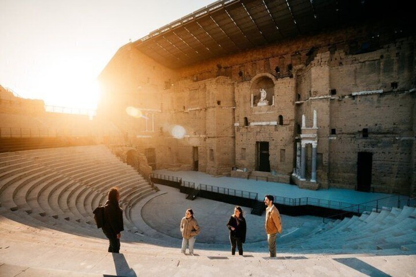 An ancient amphitheater with tiered seating and a central stage, surrounded by stone walls. 1