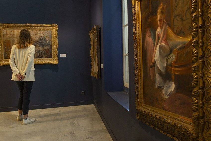 A person observing paintings in a gallery with dark walls and ornate frames. 5