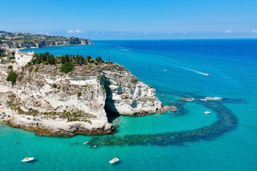 A coastal landscape with cliffs, clear turquoise waters, and boats. 5
