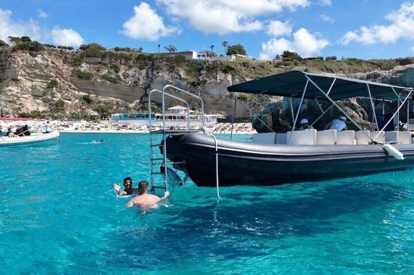 A boat docked in a clear blue sea with a rocky coastline in the background. 1