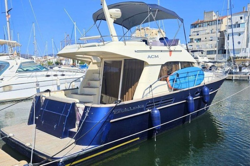 Un barco azul y blanco amarrado en un puerto deportivo, con otros barcos y edificios al fondo. 5