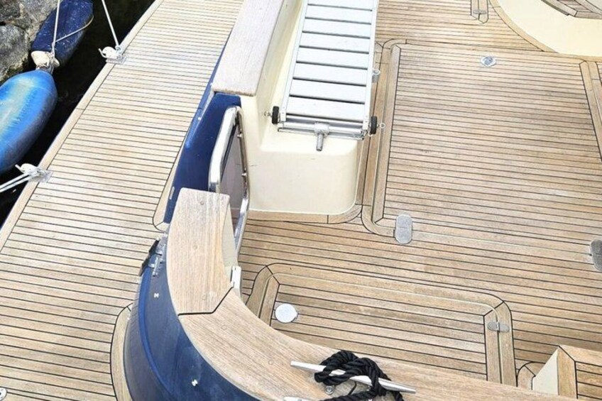 Cubierta de barco de madera con un bote azul, un flotador blanco y una cuerda. 2