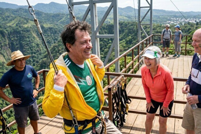 A person in a yellow jacket and green shirt on a wooden platform with a scenic view of mountains in the background. 3