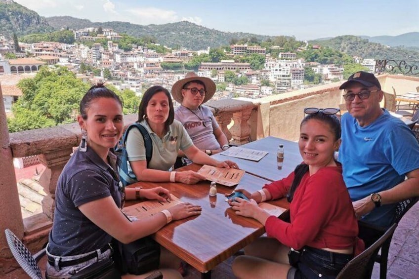 A group of people seated at an outdoor table with a view of a town and mountains in the background. 3