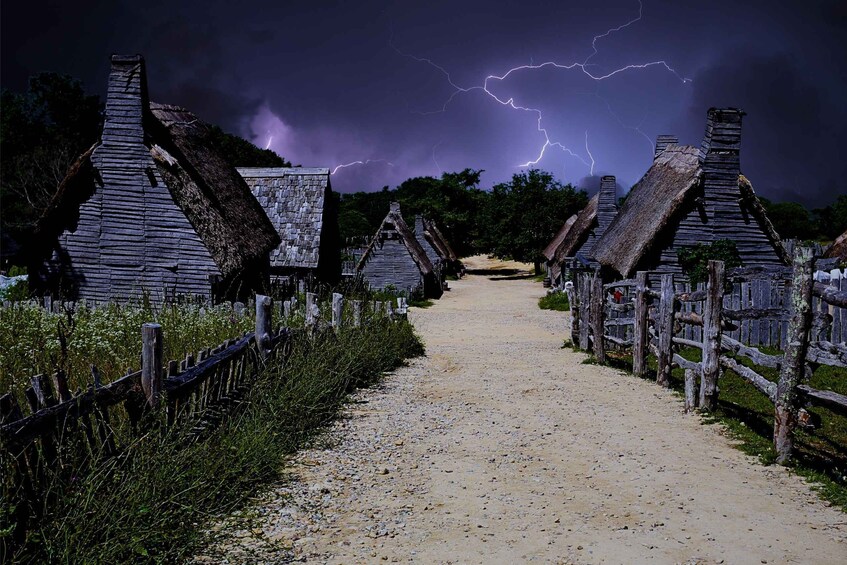 A rural path flanked by thatched-roof cottages under a stormy sky. 2
