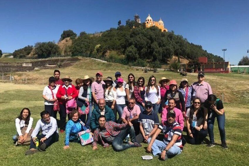 A group of people posing on a grassy field with a hill and a building in the background. 1