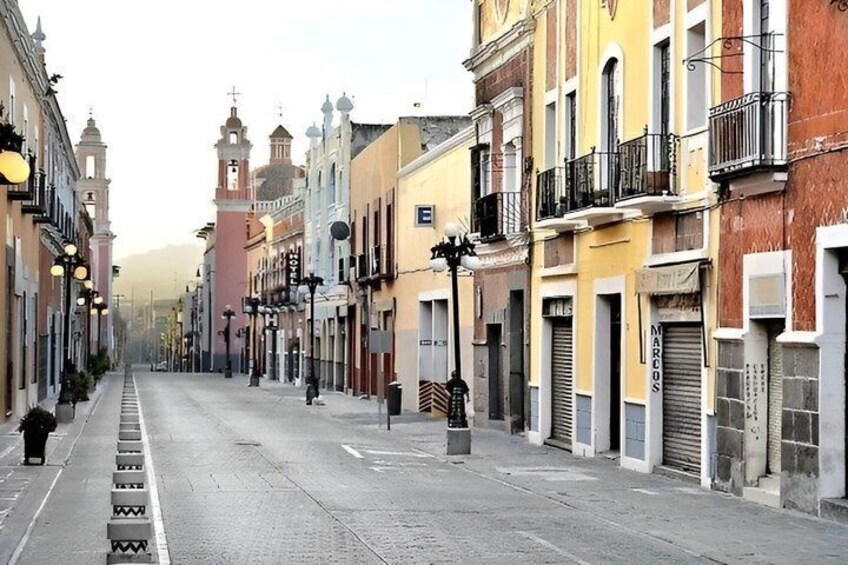 A quiet street lined with colorful buildings, a clock tower, and a clear sky. 5