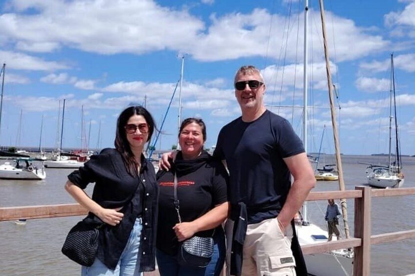 Three people standing by a dock with sailboats in the background. 1