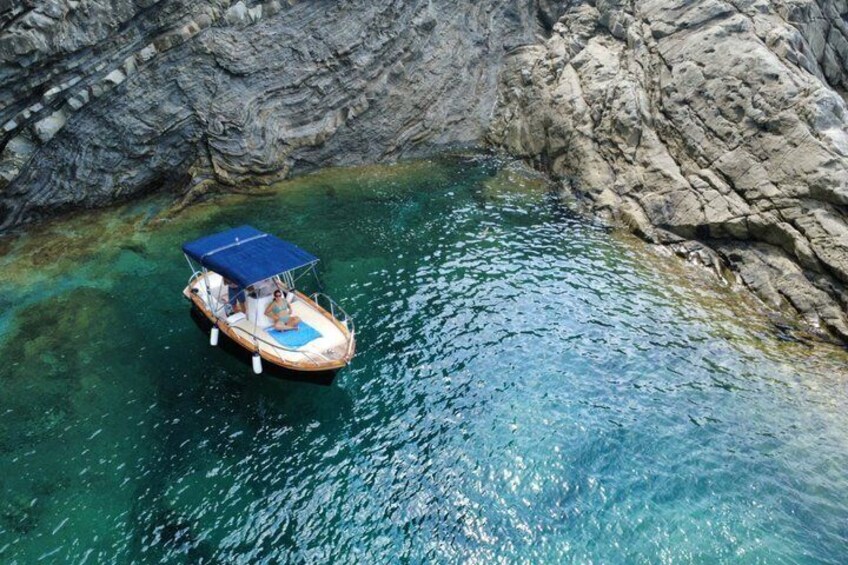 A boat with a blue canopy anchored near a rocky shoreline in clear water. 4