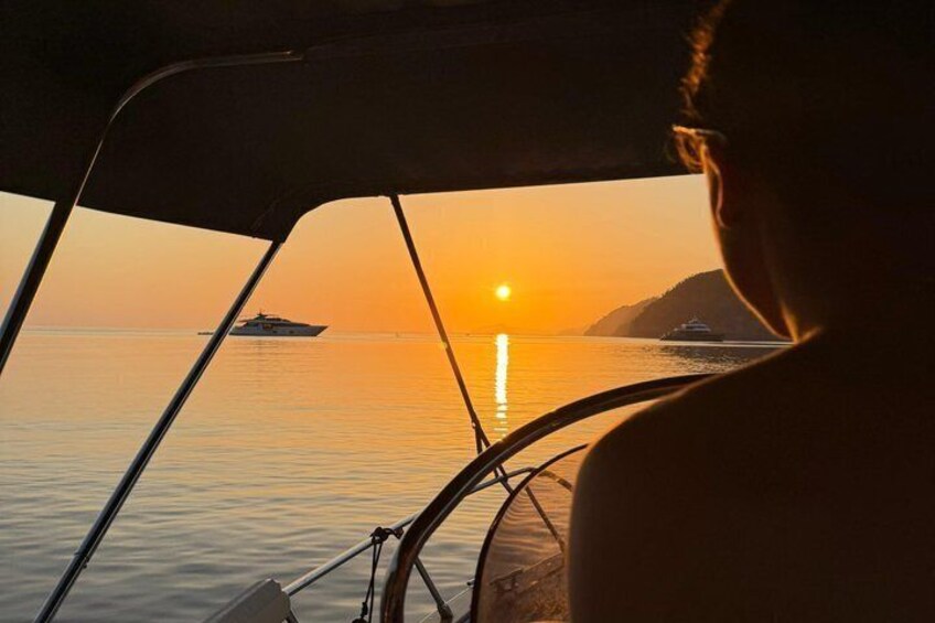 A sunset over calm waters with a boat and a distant island. 2