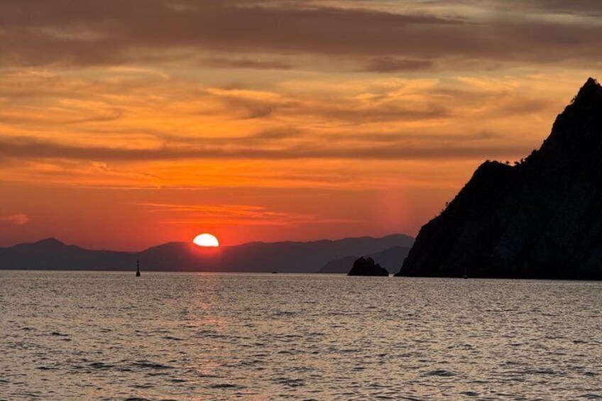 A sunset over a calm sea with a silhouette of a mountain and a buoy. 1