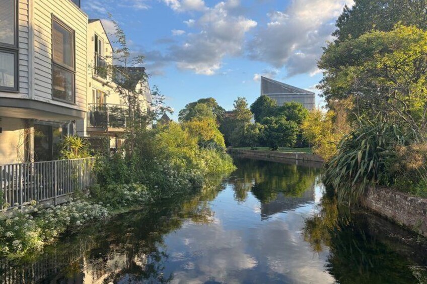 A calm river with buildings on one side and trees on the other. 5