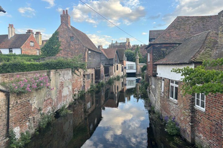 A narrow canal flanked by brick houses with a clear reflection in the water. 2