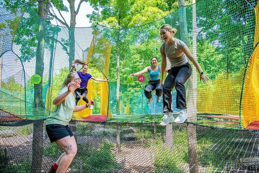 People jumping on trampolines in an outdoor netted area with trees in the background. 1