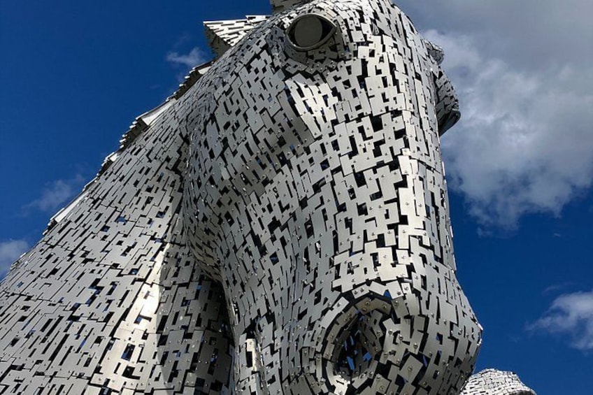 A large, intricate sculpture resembling a lion's head, made of interlocking metallic pieces, set against a clear blue sky. 5