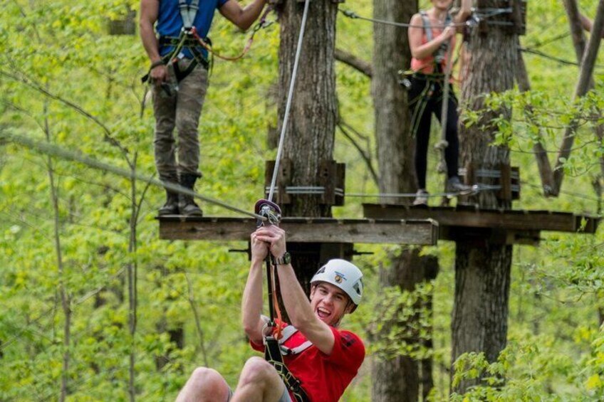 A person in a red shirt and helmet on a zip line, with another person assisting on a platform. 5