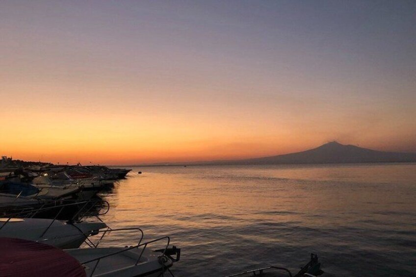 A calm sea at sunset with boats docked on the left and a mountain in the background. 3