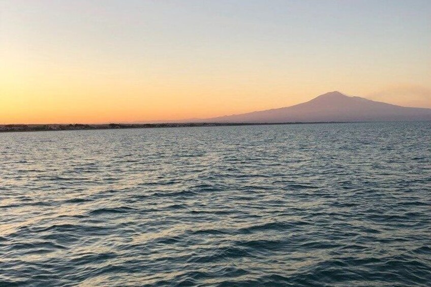 A calm sea at sunset with a mountain in the distance. 2