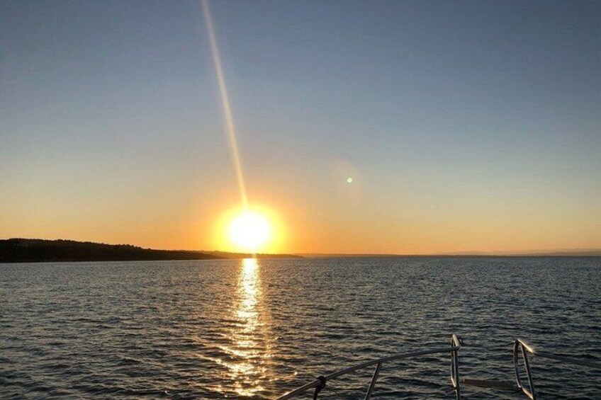 A sunset over a calm sea with a boat's railing in the foreground. 4