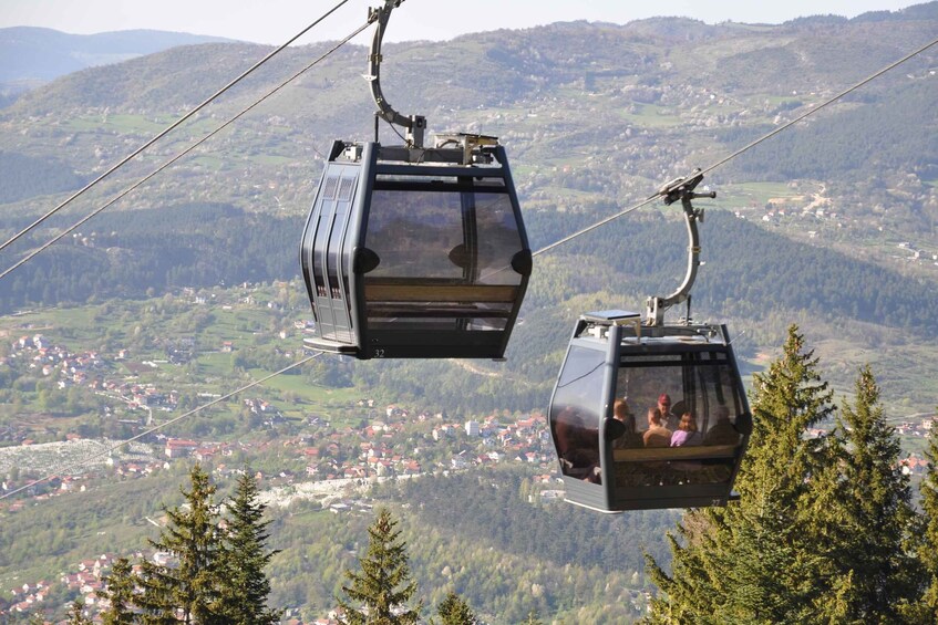 Two cable cars suspended over a mountainous landscape with a town below. 2
