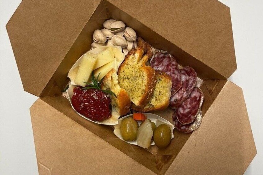 An open box containing a charcuterie board with various cheeses, nuts, olives, and cured meats. 1